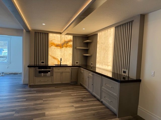 The same basement bar corner finished with driftwood-stained cabinetry, fluted slat walls and backlit onyx panels