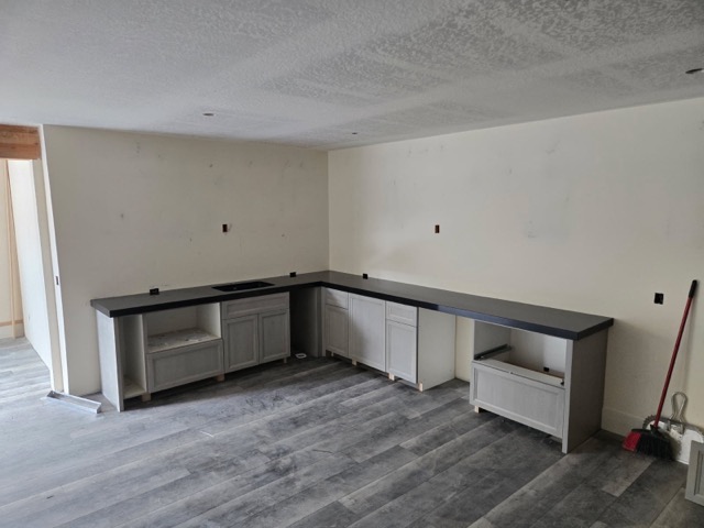 Basement bar mid-installation with unstained cabinet boxes set on shims and black quartz countertops already in place