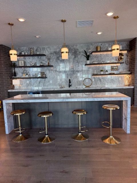 Commercial back bar with black flat-panel cabinets, brass hardware and a book-matched stone slab backsplash