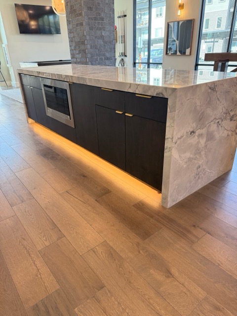 Matte black slab-front bar island with brass edge pulls, a mitred marble waterfall top and LED toe-kick lighting