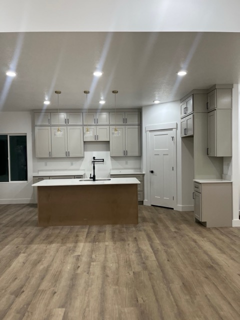 Greige shaker upper cabinets with a black pot filler and white quartz counters flanking a stained wood island