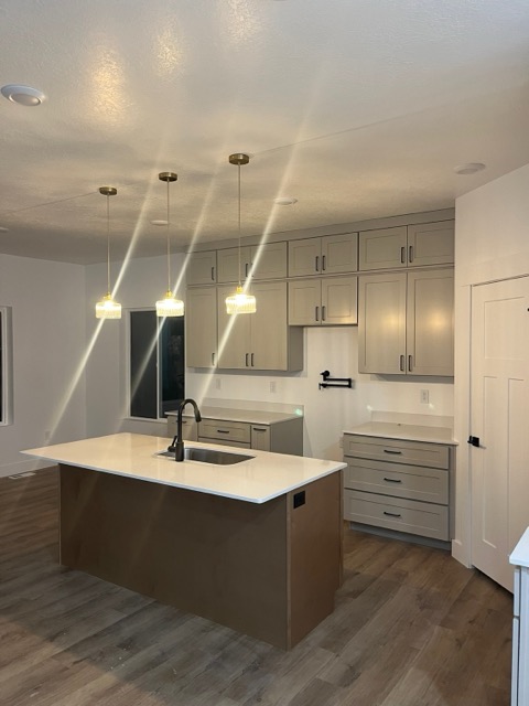 Stained wood kitchen island with a white quartz top, black gooseneck faucet and three fluted glass pendants