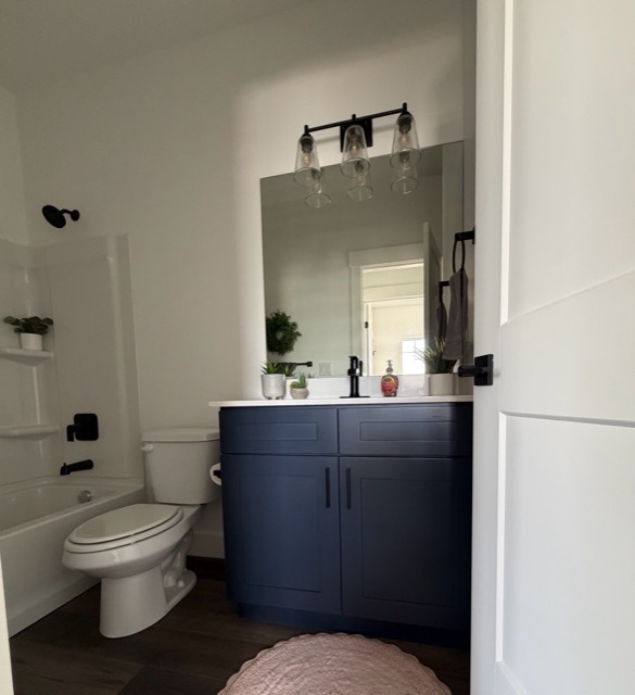 Navy blue shaker bathroom vanity with a white quartz top, frameless mirror and black three-light fixture