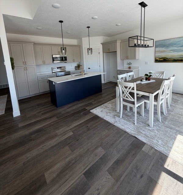 Greige shaker kitchen with a navy island and brass hardware, open to a dining area with black lantern pendants
