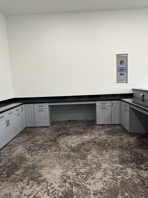 Grey shaker garage and workshop cabinetry with a black granite countertop, desk bay and stainless utility sink