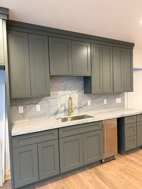 Deep hunter-green shaker wet bar with a veined quartzite countertop, gold gooseneck faucet and undercounter beverage fridge