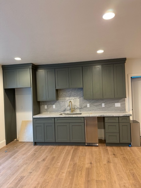 Hunter-green shaker wet bar wall with a full-height quartzite slab backsplash and stainless bar sink