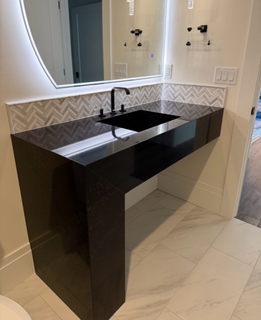 Modern basement bath with a floating black quartz vanity, backlit LED mirror and marble-look porcelain tile