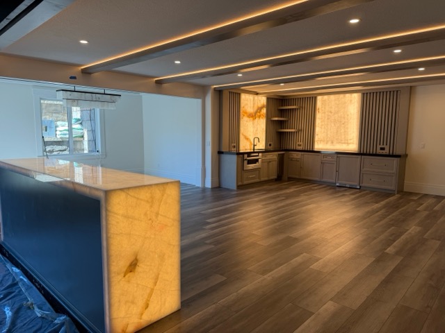Basement entertainment room with a backlit onyx waterfall bar island, driftwood-stained cabinetry and LED-lit ceiling beams