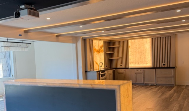 Basement theater and bar room with LED-lit coffered ceiling beams and a glowing onyx bar island