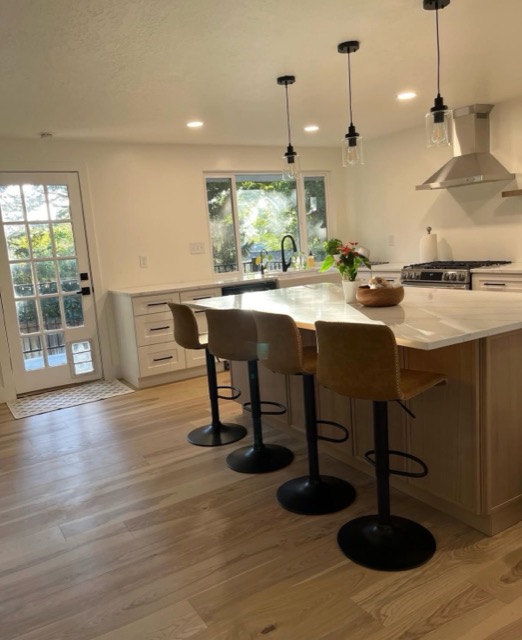 White shaker kitchen with a stainless chimney hood, walnut floating shelf and white quartz countertops
