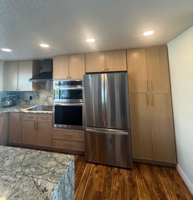 Rift white-oak cabinetry with stainless double wall ovens and a floor-to-ceiling pantry beside a granite-clad cooking wall