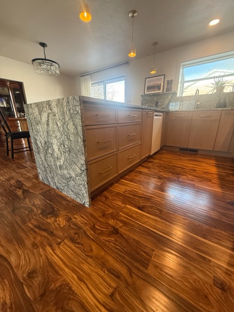 Grey-green granite waterfall peninsula with rift white-oak cabinetry and long brass bar pulls