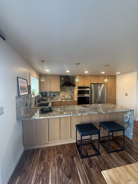 Rift white-oak kitchen with a grey-green granite waterfall peninsula, full-height granite backsplash and dark acacia floors