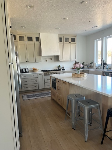 White oak kitchen island with a white quartz top and metal counter stools facing greige shaker cabinets