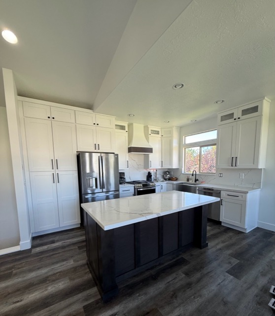 Vaulted-ceiling kitchen with white shaker cabinetry, a dark espresso island and grey wood-look plank flooring
