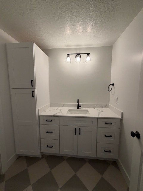 White shaker bathroom vanity with a linen tower, quartz countertop, matte black fixtures and checkerboard tile floor