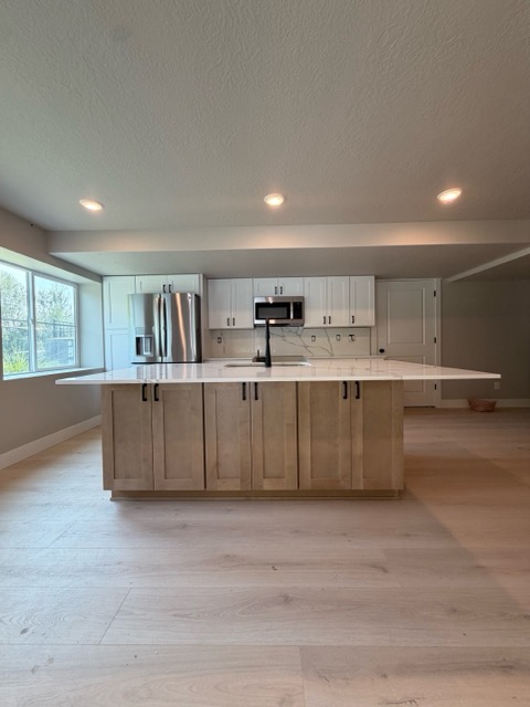 Natural maple shaker island with deep drawer storage and a white quartz waterfall edge beside white perimeter cabinets