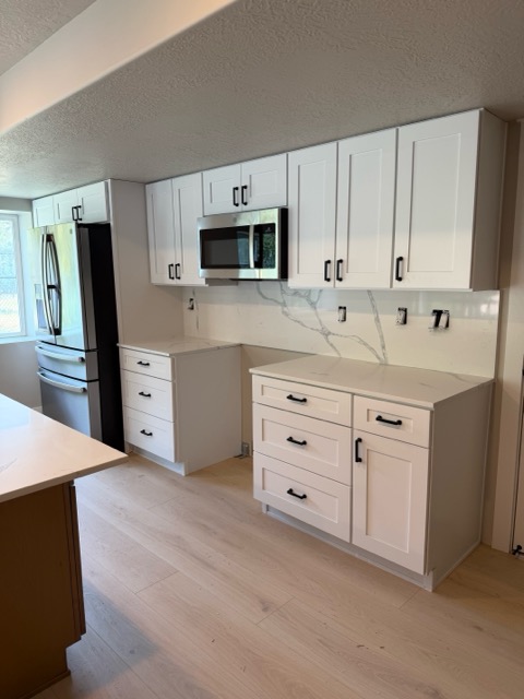 White shaker elevation with a stainless wall oven and refrigerator and quartz backsplash carried to the ceiling